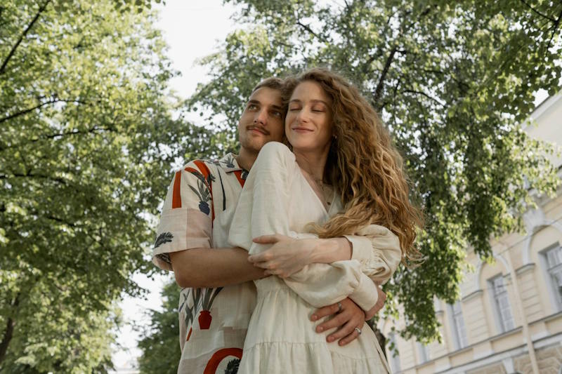 Giovane coppia si abbraccia con affetto in un parco, sorridendo con serenità, simbolo di una relazione sana e duratura