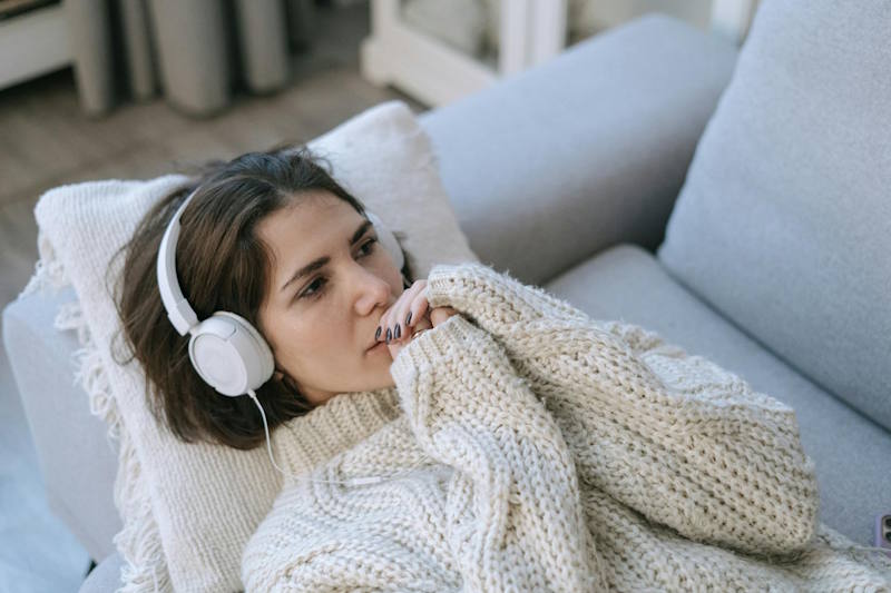 Femme pensive allongée sur un canapé en pull chaud, écoutant de la musique au casque, illustrant la réflexion sur les erreurs à éviter en amour