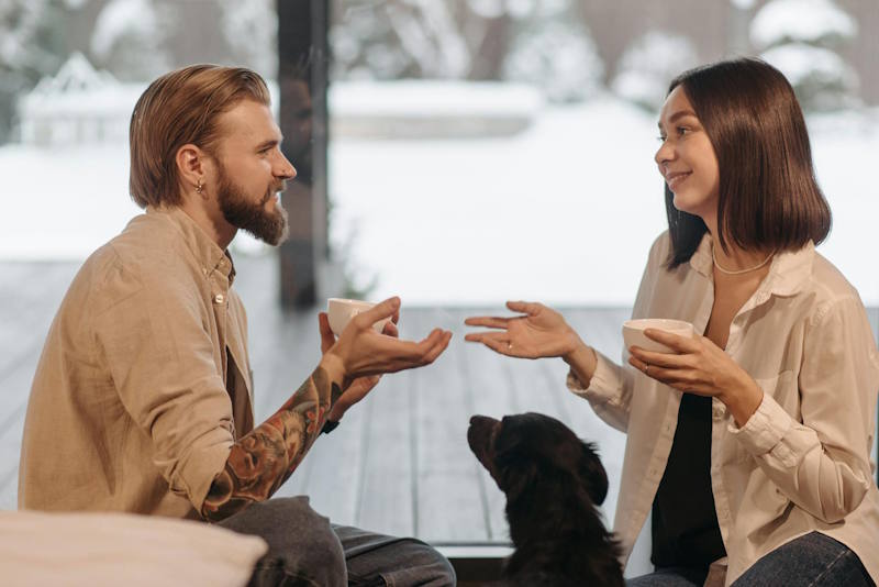 Couple souriant en pleine conversation dans un cadre chaleureux, avec un animal de compagnie entre eux, illustrant l’importance d’une communication positive après une période de silence radio