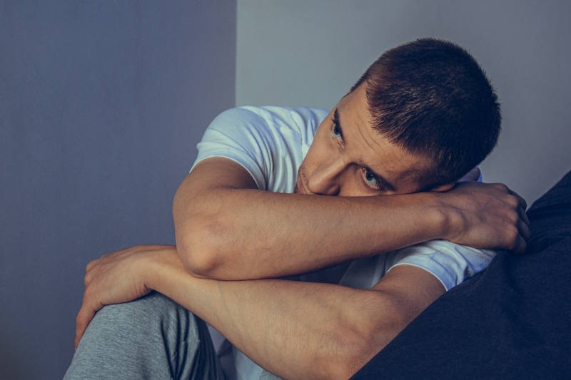 Hombre joven sentado solo, con expresión triste y pensativa, representando el impacto emocional de la codependencia y la búsqueda de respuestas sobre su origen