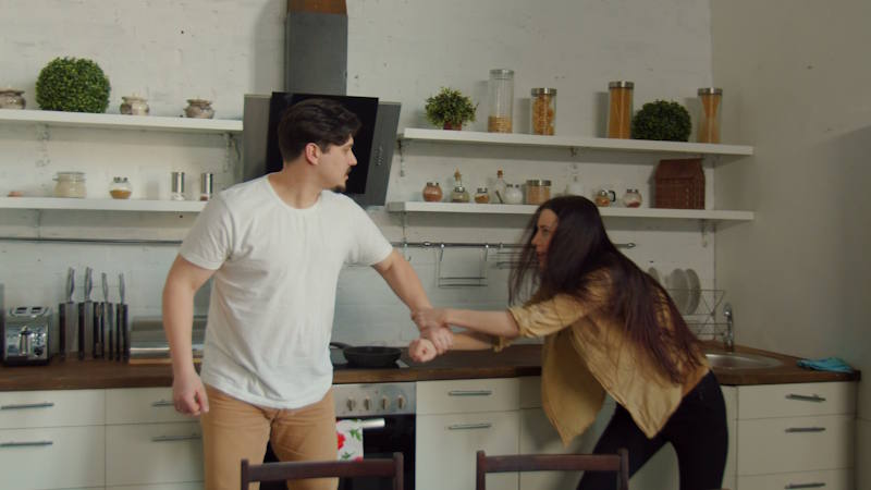 Couple en pleine dispute intense dans la cuisine, femme tenant le bras de l’homme, montrant tension et conflit, illustrant la différence entre abus émotionnel et conflits courants dans le couple.