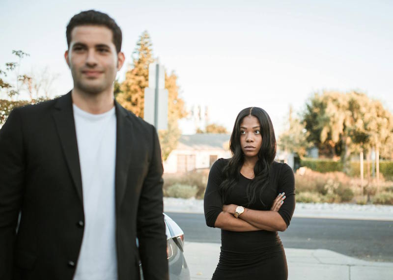 Couple en pleine dispute dans la rue, femme aux bras croisés et regard inquiet, homme qui s’éloigne indifférent, illustrant la difficulté à reconnaître l’abus émotionnel dans une relation.